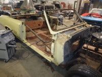 Yellow convertible car undergoing restoration in a cluttered garage, steel frame visible.