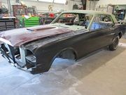 Classic black Mustang in a body shop, partially disassembled with a different-colored hood and roof during restoration.