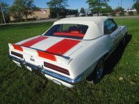 White convertible classic car with red racing stripes on trunk, parked on grass.