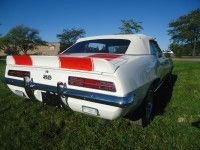 White 1969 Chevrolet Camaro SS convertible with red stripes on the rear, parked on grass.