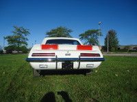 White vintage car, rear view on grass, red tail lights, blue sky.