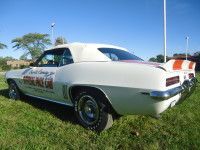 White vintage convertible car on grass, racing stripes on rear, blue sky.