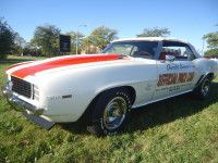 White 1969 Chevrolet Camaro with red racing stripes, parked on grass. 
