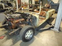 Partially disassembled convertible car, engine visible, in a workshop. Yellow body, exposed frame, on a lift.