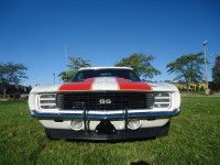 White and red 1969 Chevrolet Camaro SS muscle car parked on grass, with a blue sky background.
