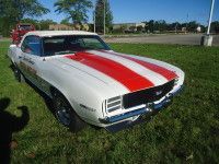 White and red 1969 Chevrolet Camaro on grass, parked near a parking lot.