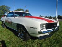 White vintage Camaro with red stripe on hood, parked on grass.