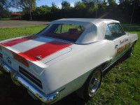 White and red 1969 Chevrolet Camaro convertible with racing stripes, parked on grass.