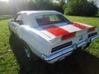 White and red 1969 Chevrolet Camaro convertible with racing stripes, parked on grass.