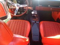 Interior of a vintage orange car with matching seats, wooden steering wheel, and black console.