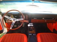 Interior of a classic orange and white car with wooden accents and a chrome steering wheel.