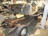 Car frame with attached engine, body shell detached. In a garage setting.