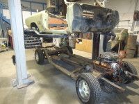 Car body lifted, chassis below; car repair shop. Black and tan parts; steel lift.