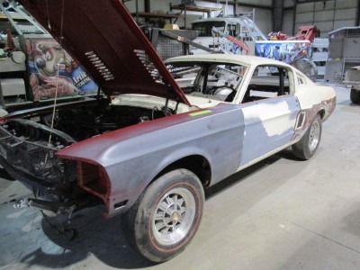A classic white and burgundy Mustang fastback in a garage under restoration, with the hood open.