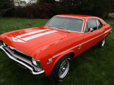 Red 1969 Chevrolet Nova SS with white stripes on a grassy lawn.