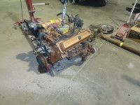 Engine being lifted by a hoist in a garage. Gold valve covers, brown engine. Tools and concrete floor.
