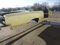Yellow truck bed frame outdoors on stands.