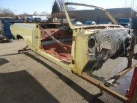 Yellow convertible car body frame, on a metal stand, outdoors.