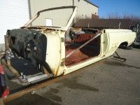 Yellow convertible car body frame, stripped down in an outdoor setting.