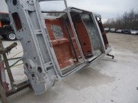 Bare metal car chassis on a stand outdoors, painted gray with rust-colored interior.