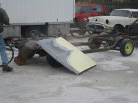 Person working on a car frame. In the background is a white truck and a classic white car.