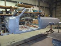 Partially assembled gray classic car body in a workshop.