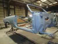 Bare, light-blue car frame in a workshop, supported by stands, revealing the interior structure.