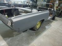 Partially restored gray convertible car body, yellow wheel, in a workshop.