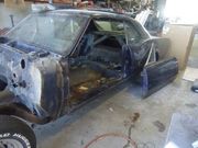 Partially disassembled dark blue classic car in a garage, showing the interior and roll cage.
