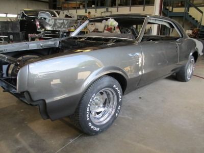 A gray classic car undergoing restoration in a workshop, with shiny paint and chrome wheels.