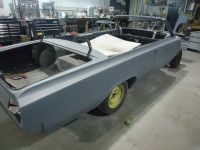 A grey, classic convertible car body in a workshop, ready for restoration. Yellow wheels.
