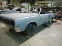 A light blue classic convertible car, in a workshop being worked on, ready for restoration.