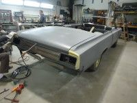 Gray convertible car in a workshop, under restoration. Person works in background.
