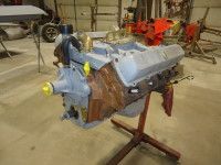 Engine block, painted gray, mounted on a red stand in a workshop.