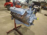 An engine, painted gray, is mounted on a red stand inside a garage.