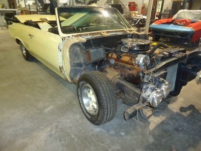 Yellow convertible car in a garage undergoing restoration, with the front engine components exposed.