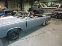 Convertible car undergoing restoration in a workshop. Gray primer, black wheels, yellow accents.