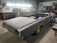 A light gray convertible car undergoing restoration in a workshop. The car is partially assembled with an open top.
