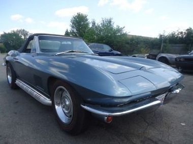 Blue convertible Corvette parked on pavement. Chrome details, black convertible top.