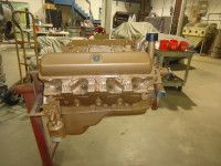 Tan engine on a red stand in a workshop, with other equipment and covered items in the background.