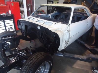 White classic car mid-restoration in a garage, with body and black chassis separated and interior exposed.