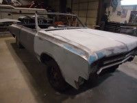 Old convertible car, partially dismantled in a workshop, undergoing restoration. Gray metal body, missing parts.