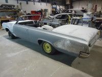 Partially assembled light blue convertible car in a garage with yellow wheels.