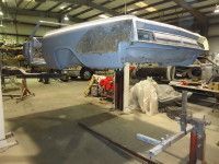 A car frame undergoing restoration is suspended in a workshop.