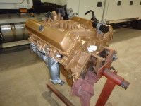 Bronze-painted car engine on a red engine stand, inside a garage or workshop.