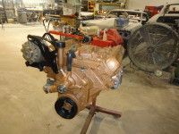 Bronze-colored car engine on a stand in a workshop, with black and red accents.