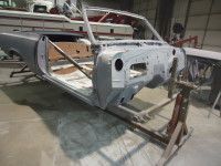 Partially assembled gray classic car body on a metal frame inside a workshop.