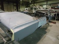 Car body in a workshop, primed and partially assembled. Boats in the background.