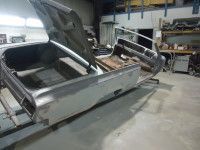 Partially restored car in a workshop, trunk open, metal finish.