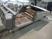 Partially assembled classic car body in a workshop. Gray, rusty metal.